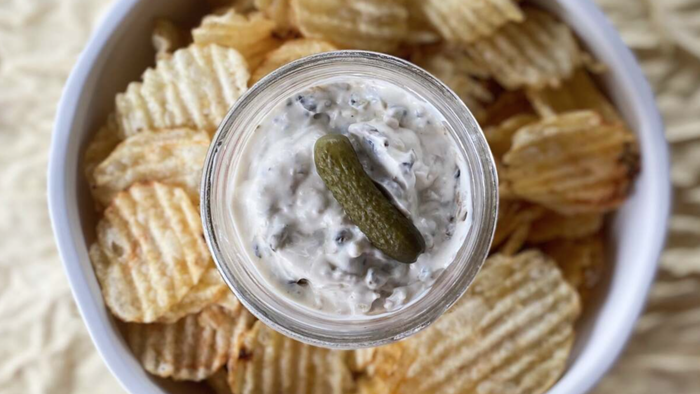 A small bowl of pickle dip surrounded by a layer of crispy chips.
