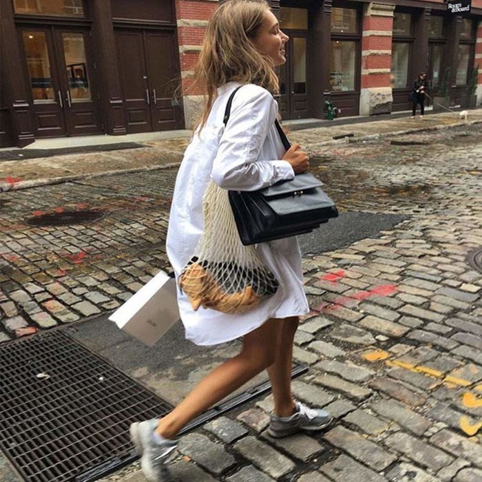 A model strolling down a city street, carrying a beige shopping bag filled with various items