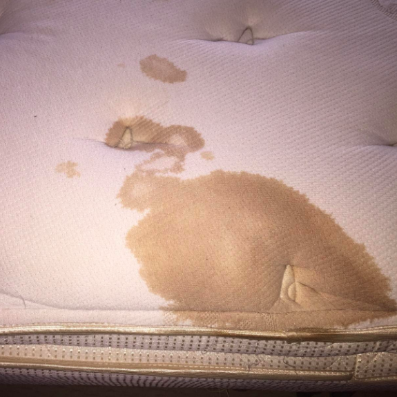 a reviewer's mattress with a large brown stain visible before cleaning