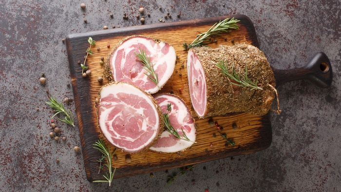 A slice of pancetta resting on a cutting board, garnished with fresh rosemary.