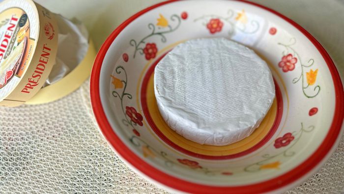 A wheel of brie resting in a microwave-safe bowl, ready to be heated.