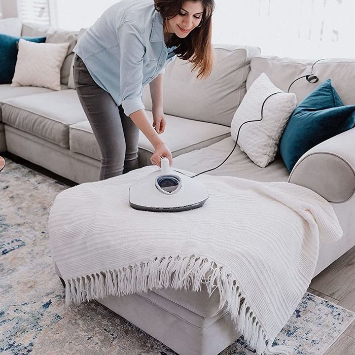 A person is using a vacuum cleaner to freshen up a throw blanket that is plugged in.