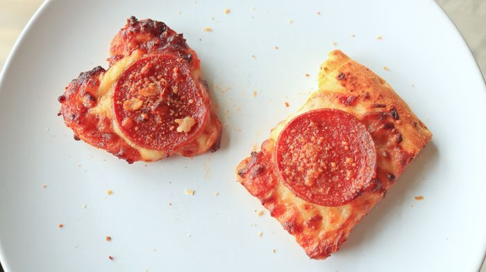 A small, heart-shaped pizza topped with pepperoni alongside a small rectangular slice.