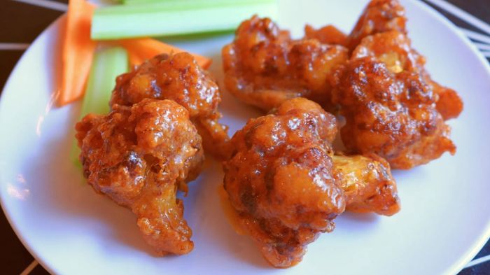Buffalo cauliflower 'wings' served on a plate with fresh carrot and celery sticks.