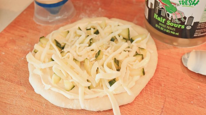 A pizza crust coated with mayonnaise, topped with pickles and cheese.
