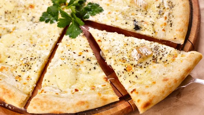 A white pizza with a slice being pulled away from the rest.