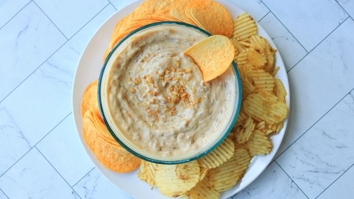 A bowl of onion dip surrounded by chips on a plate.
