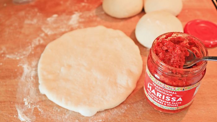 A jar of harissa rests next to a small round of pizza dough.
