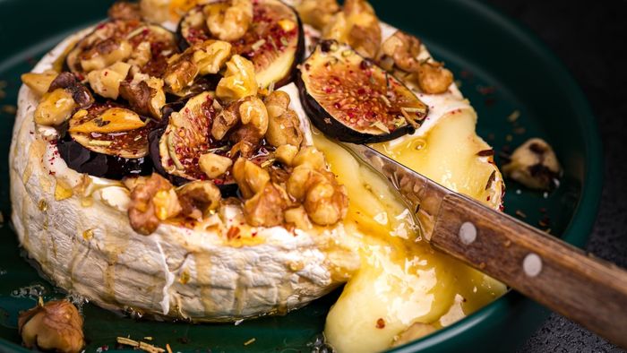 A close-up view of gooey brie cheese adorned with walnuts and figs.