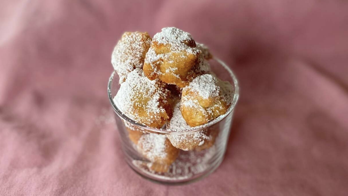A glass of fried dough pieces dusted with powdered sugar.