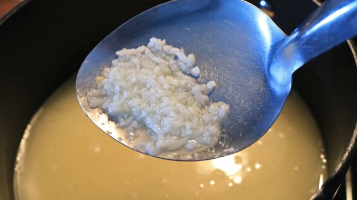A spoon scooping up broken rice from a pot filled with broth.