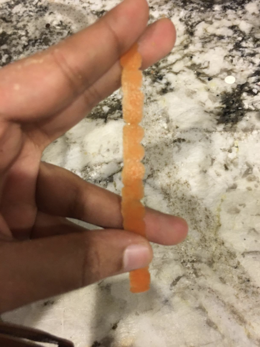 A reviewer holding a delicate, razor-thin strip of carrot peeled using the peeler