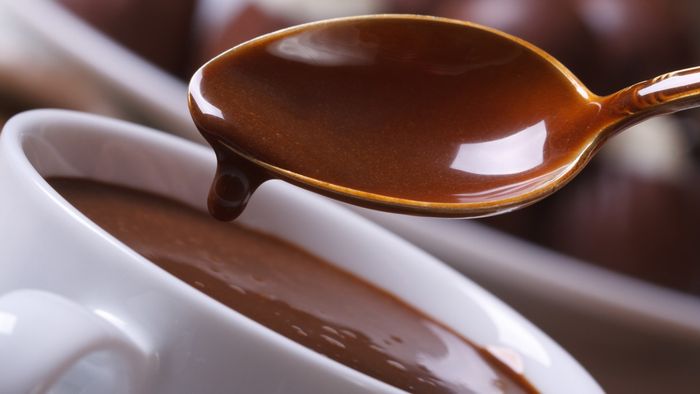 A spoon lifting a rich, velvety hot chocolate from a steaming mug.