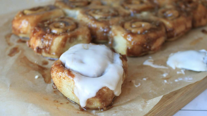 A plate of freshly baked cinnamon rolls, with one topped generously with icing.