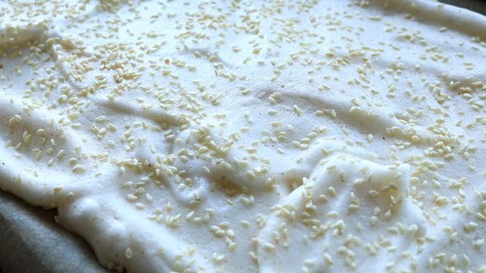 Meringue topped with sesame seeds spread out on a baking tray.