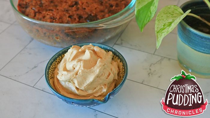 A small bowl of frosting placed next to a potted plant and a bowl of brown cake.