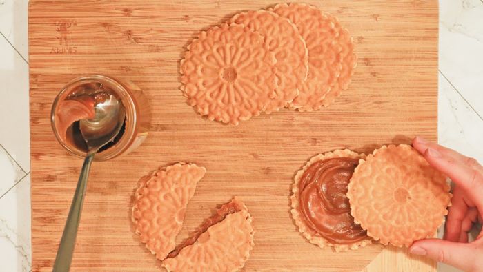 A plate of pizzelles placed on a cutting board alongside a jar of dulce de leche.