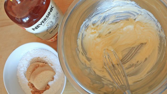 A bowl of butter sitting next to a bowl of sugar and a bottle of brandy.