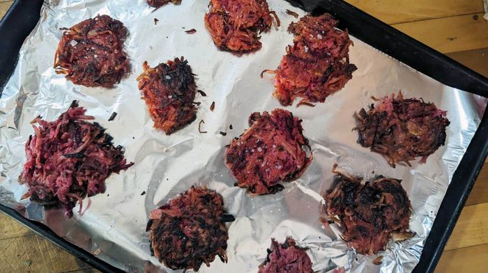 An image of crispy red flannel latkes arranged on a cookie sheet.