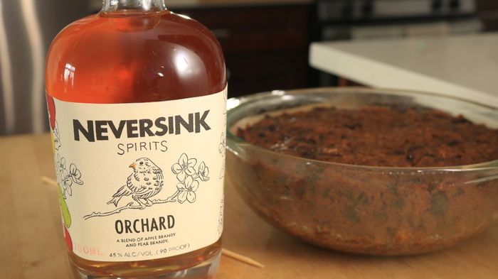 A bottle of brandy sits beside a cake in a bowl.