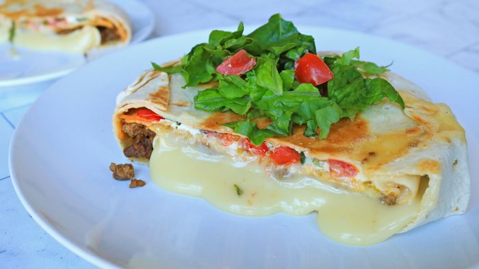 A slice of Crunchwrap Supreme-inspired baked brie, with melted cheese spilling onto the plate.