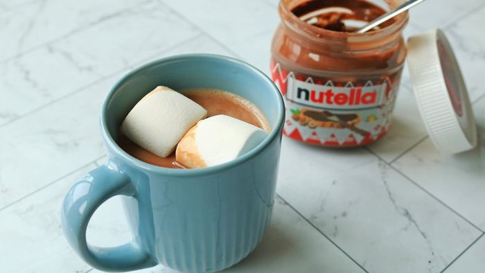 A steaming mug of hot chocolate paired with an open jar of Nutella.