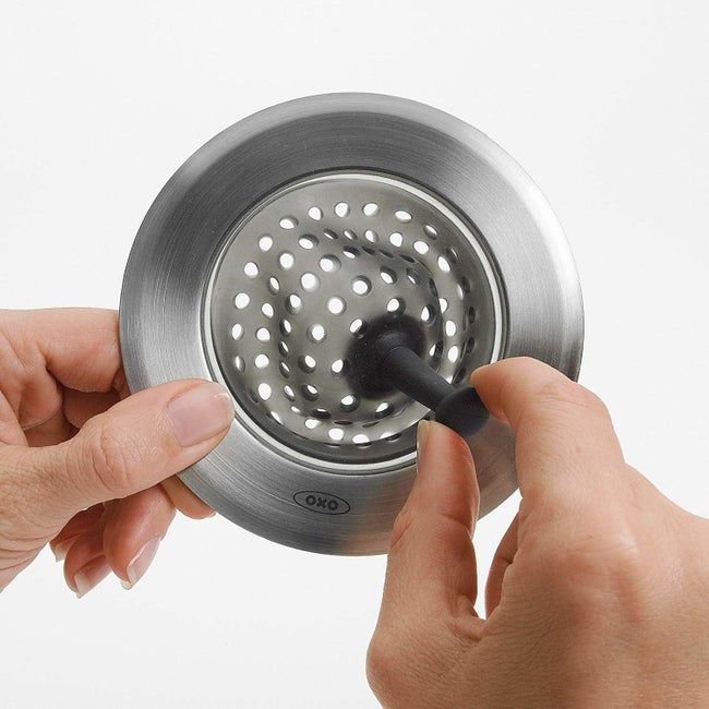 A person grips a sink strainer with a knob that you can adjust to help remove food remnants from it.