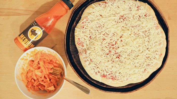 Pizza served with a bottle of buffalo sauce and a bowl of shredded turkey.