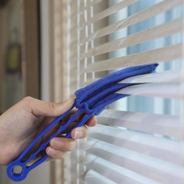 a hand using a duster to clean window blinds