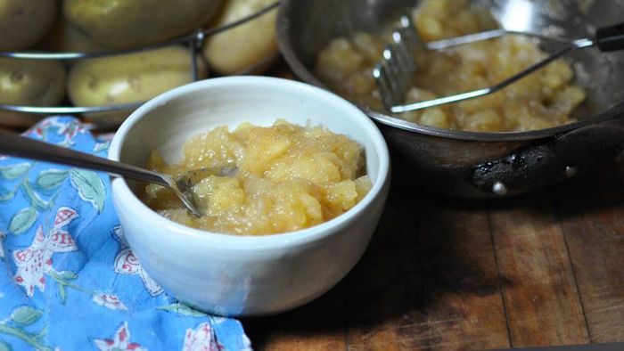 A bowl of applesauce placed next to the pot it was freshly prepared in