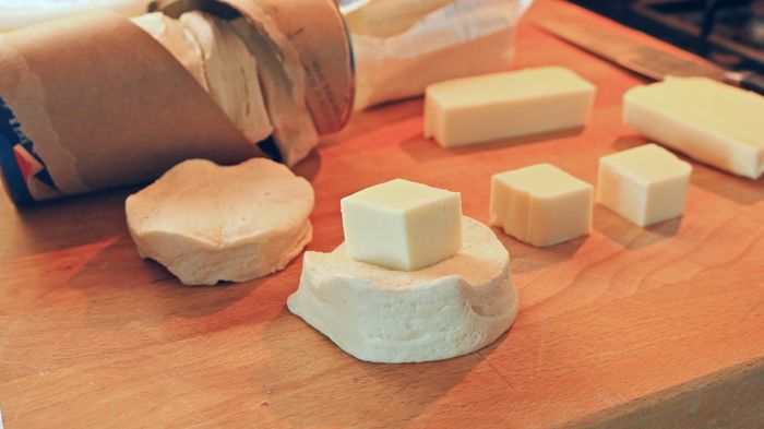 A cube of cheese resting atop a raw biscuit.