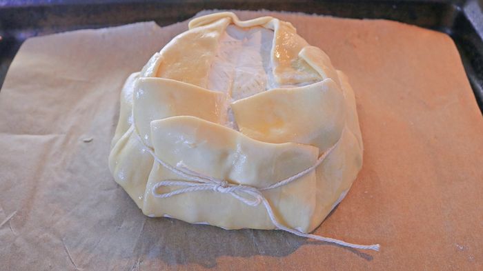 Puff pastry enveloping a brie wheel, reinforced with kitchen string for support.