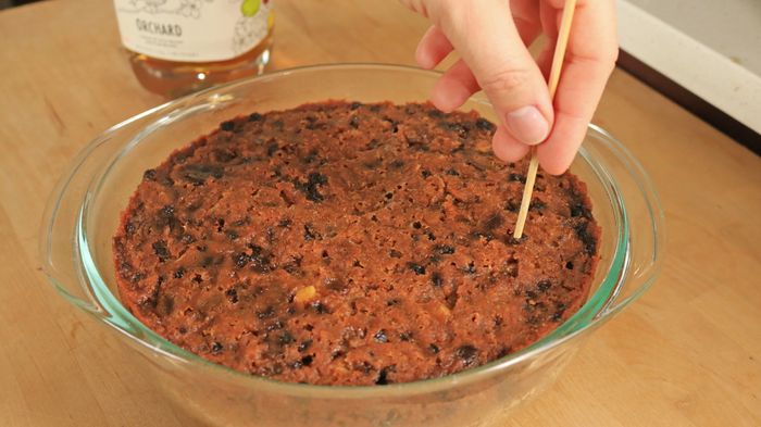 A hand uses a wooden skewer to poke a hole in the cake.