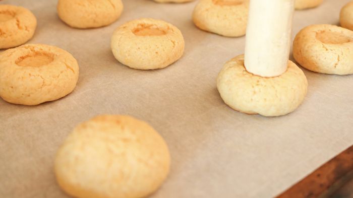 A close-up of a wine cork pressing into a cookie, along with other cookies that have an indent in the center.