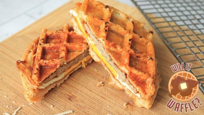 A sausage, egg, and cheese sandwich neatly sliced in half on a cutting board.
