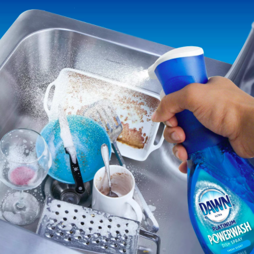 Spraying Dawn dish spray onto a sink filled with dirty dishes.