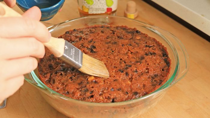 A hand uses a pastry brush to apply a coating on the top of a cake.