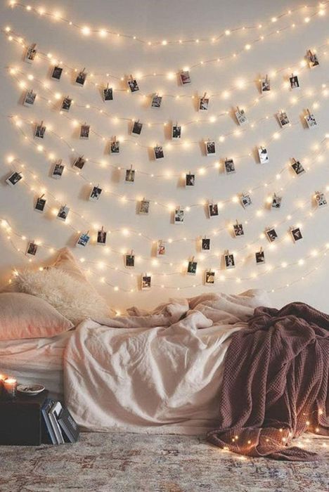 String lights with Polaroid photos clipped to them, hanging above a bed.