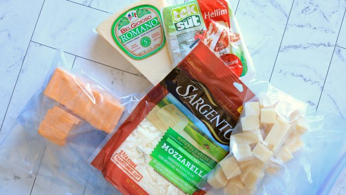 Plastic freezer bags containing cheese in various forms—bags, blocks, and slices—set on a kitchen countertop.