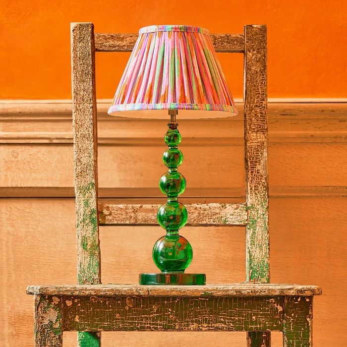 A rustic wooden chair paired with a green glass lamp featuring a vibrant, pleated lampshade, designed for a shopping feature.
