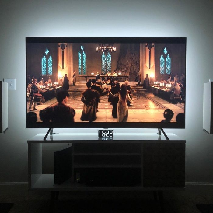 A TV screen displaying a medieval banquet scene with people dancing in a grand hall, flanked by two speaker stands, with the time showing 6:22 beneath the TV.
