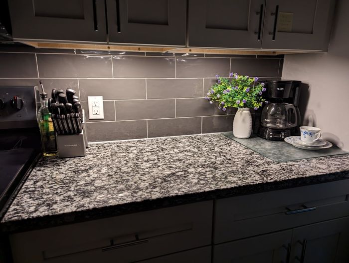 A pristine kitchen counter featuring a knife block, a bottle of olive oil, an electric coffee maker, a potted plant, and a cup with a saucer resting on a marble surface.