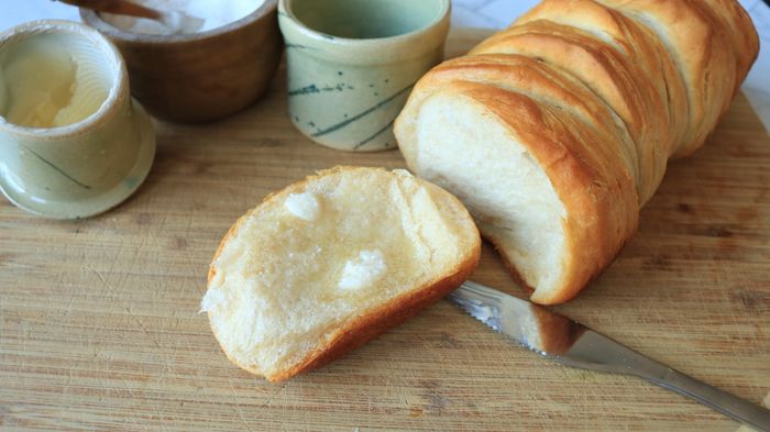 A biscuit with butter spread on it, torn from a loaf.
