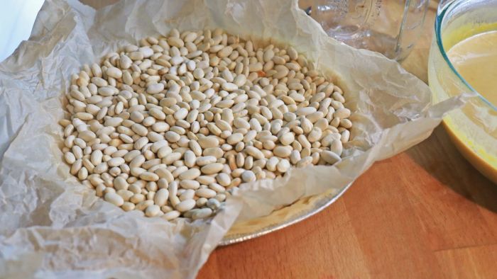 A pie crust lined with parchment paper, filled with baking beans.