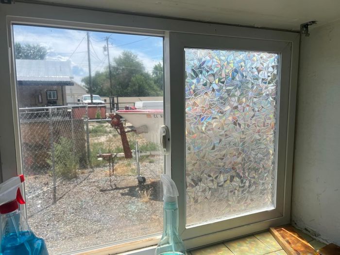 A window with one clear pane showing an outdoor scene, while another pane is covered with decorative frosted film. Cleaning supplies are placed on the windowsill.