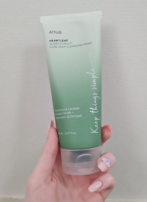 A hand holding the Anua Heartleaf 70% Pore Deep Cleansing Foam tube, adorned with nail art. Text on the tube: skincare details