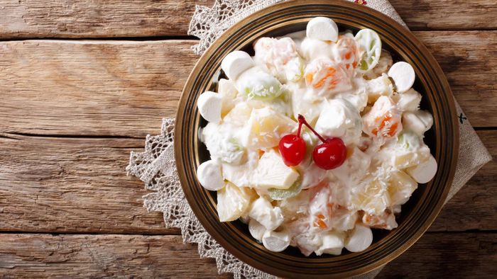 A bowl of ambrosia salad garnished with maraschino cherries.
