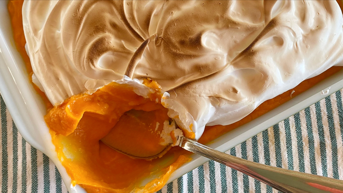 A sweet potato casserole adorned with meringue, served with a spoon.