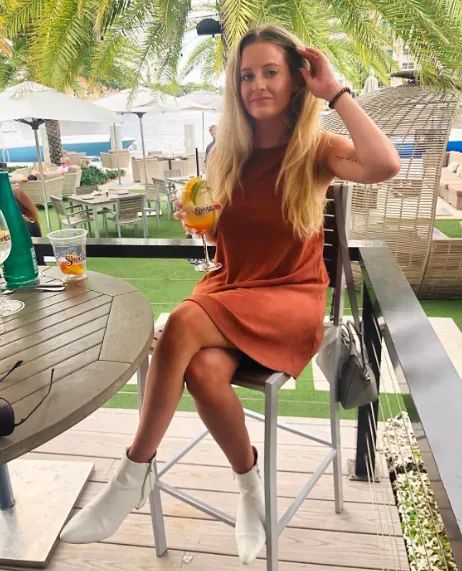 A reviewer is seen wearing white heeled booties styled with an orange dress.