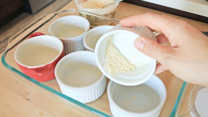 A row of ramekins coated with parmesan cheese, placed inside a casserole dish.